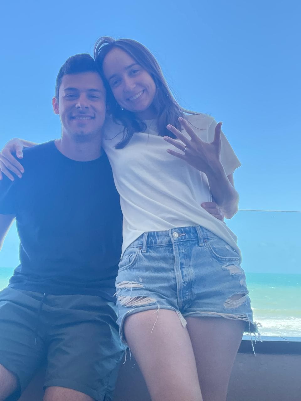 Luiza mostrando o anel de noivado em Taíba, com o mar ao fundo